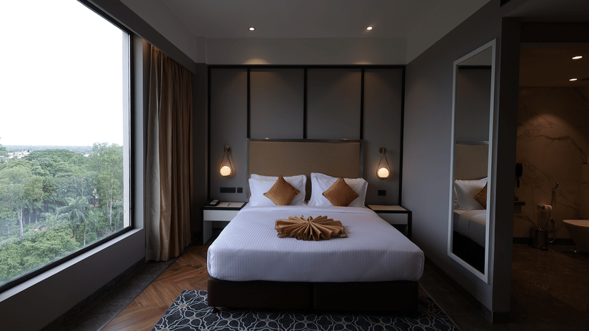Studio Suite bedroom with king bed, floor-to-ceiling window with green view and patterned carpet at Polo Hotel, Agartala.