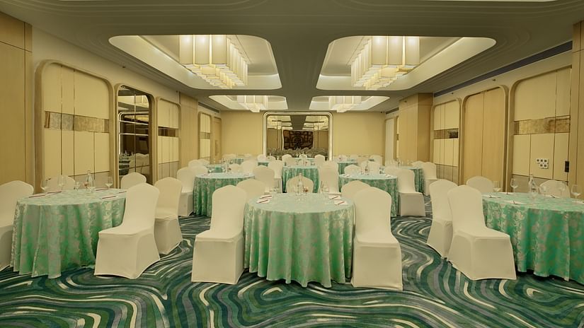Banquet room with round tables draped in light green, surrounded by white chairs. Patterned carpet and soft lighting - The Orchid Hotel, Chandigarh