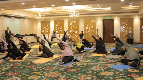 An image of a group of people performing yoga by stretching their hands  by sitting on a yoga mat at Heritage Village Resorts & Spa
