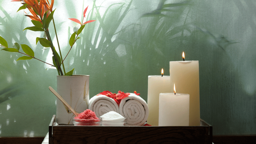 Candles and a floral arrangement set against a green wall with leafy shadows at Amanvana Spa Resort.