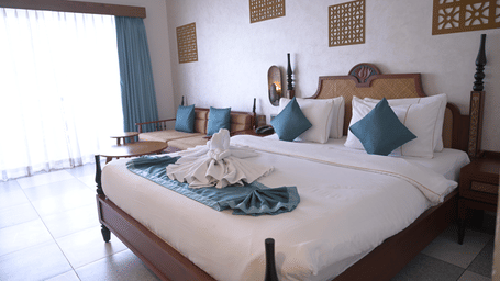 A guest room featuring a double bed with towel art, wall decorations, and a window with blue curtains at Hotel Sonar Bangla, Mayapur.