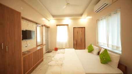 A bedroom at Shophori Wellness Retreat, Bolpur, with king size bed, wall-mounted TV, wardrobe, and window curtains.