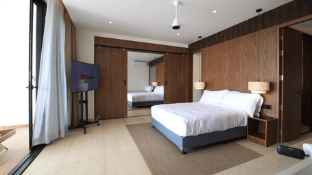 A bedroom at SUKAVI featuring a king size bed, a wall-mounted television, a ceiling fan, and large sliding glass doors that open onto a private balcony.