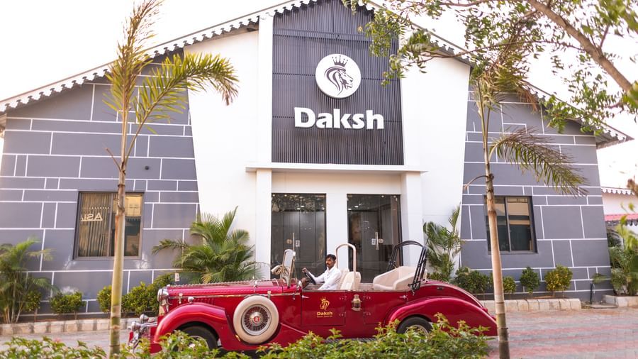 A vintage car stopped behind potted plants, with the exterior of a building standing tall in Daksh Eden Greenz, Sasar Gir.