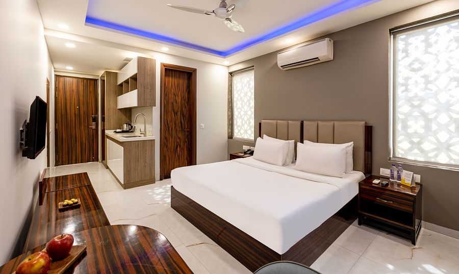 Spacious king size bed in a room with soft lighting and stylish wooden furniture at Hotel Bawa, Gurgaon.