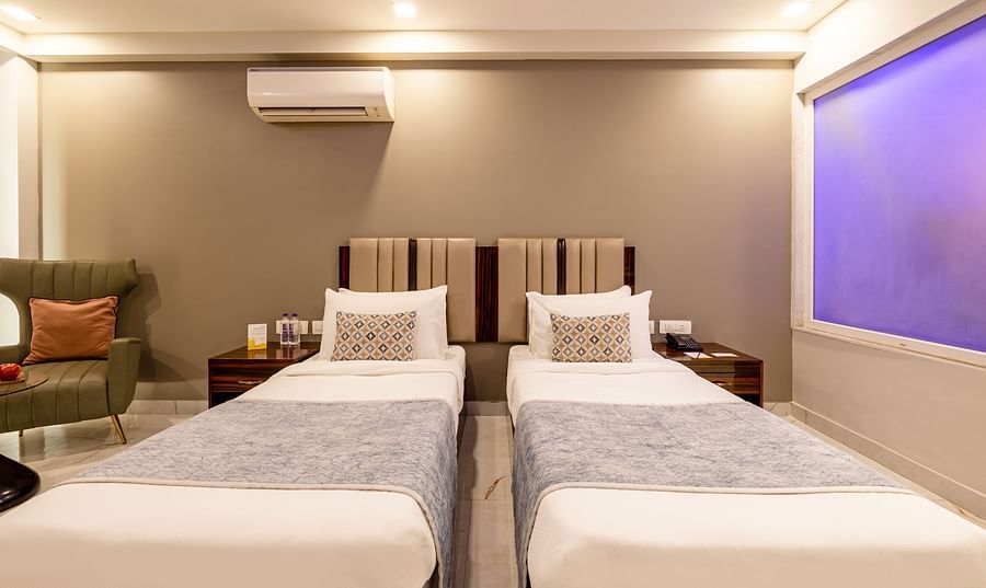 Twin beds in a room with soft lighting and a sofa chair at Hotel Bawa, Gurgaon.