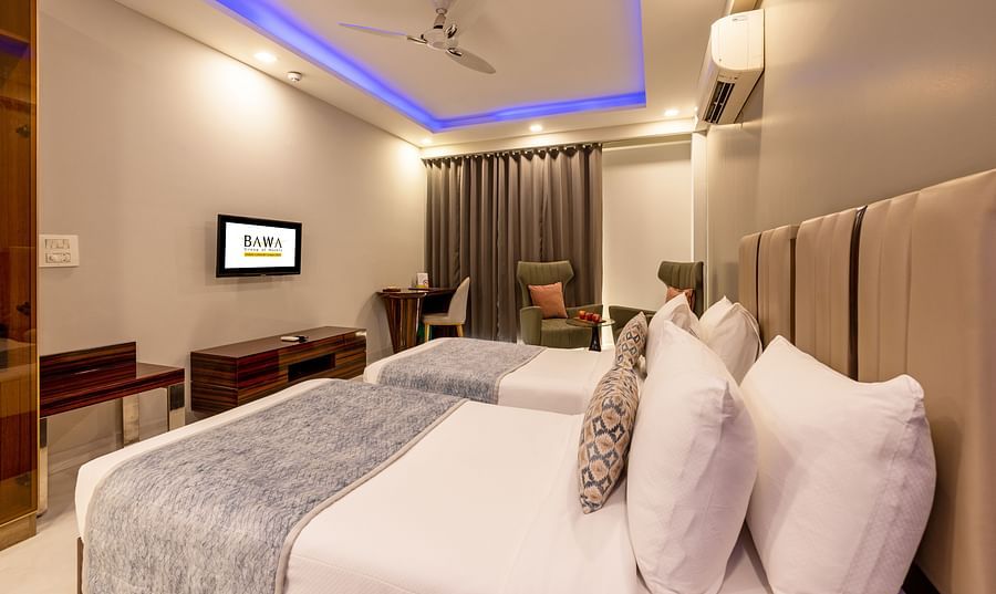 Twin beds in a room with ceiling lights and wooden furniture at Hotel Bawa, Gurgaon.