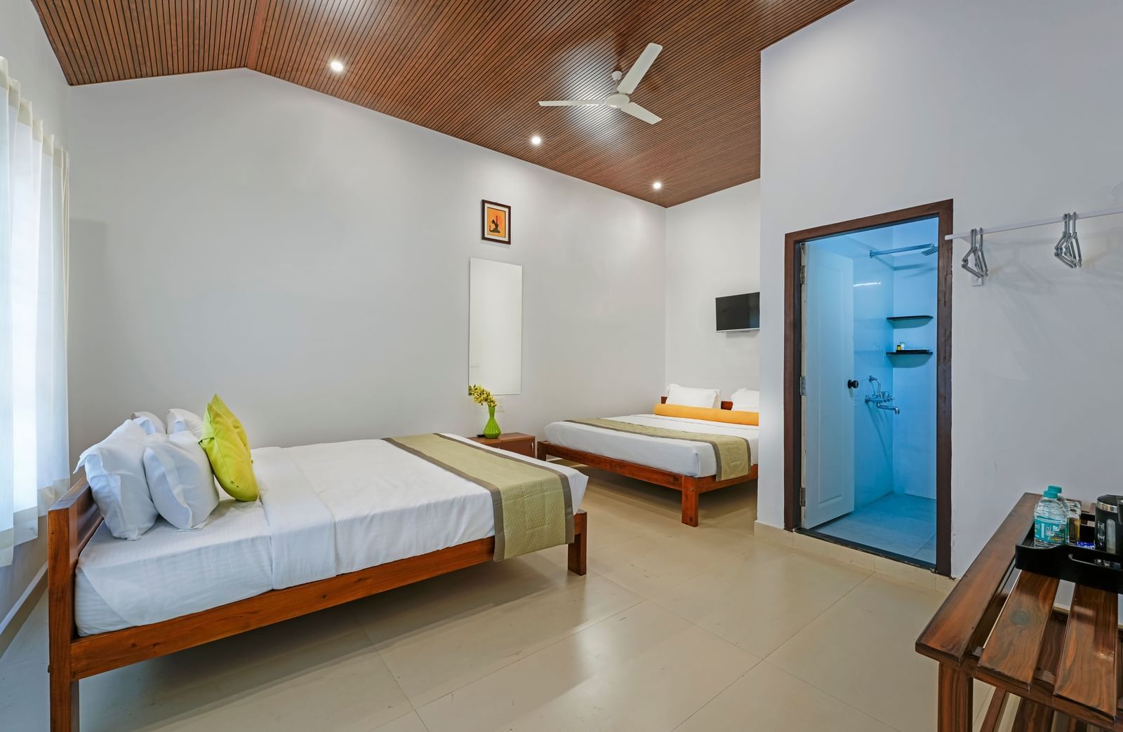 A bright and airy family room at Bhuthanakadu Retreat, featuring two comfortable beds with vibrant green and white bedding, and a ceiling fan.