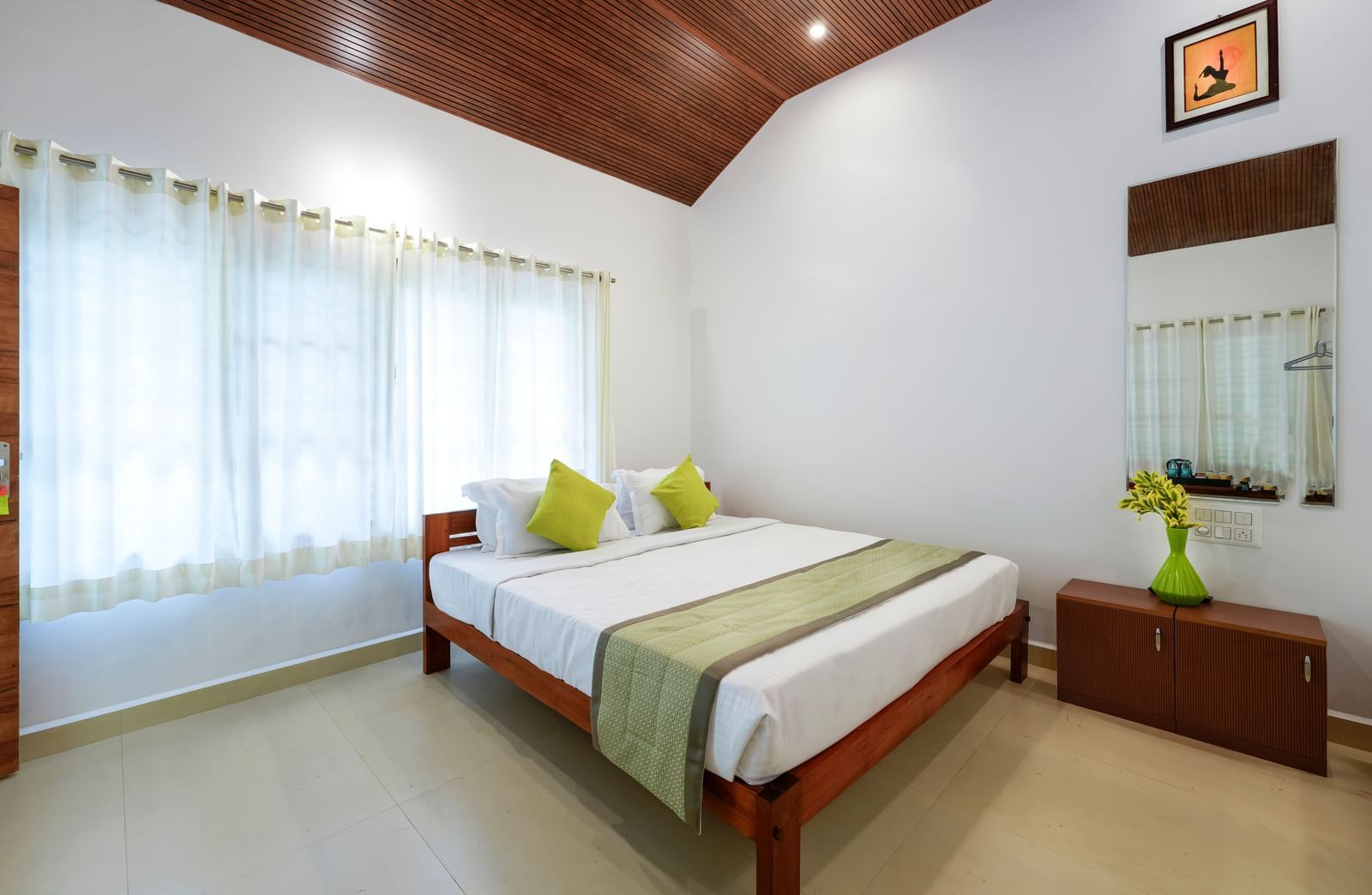 A spacious family room at Bhuthanakadu Retreat, highlighting a double bed and a single bed with bright pillows, large windows with sheer curtains, and a high-pitched wooden ceiling.