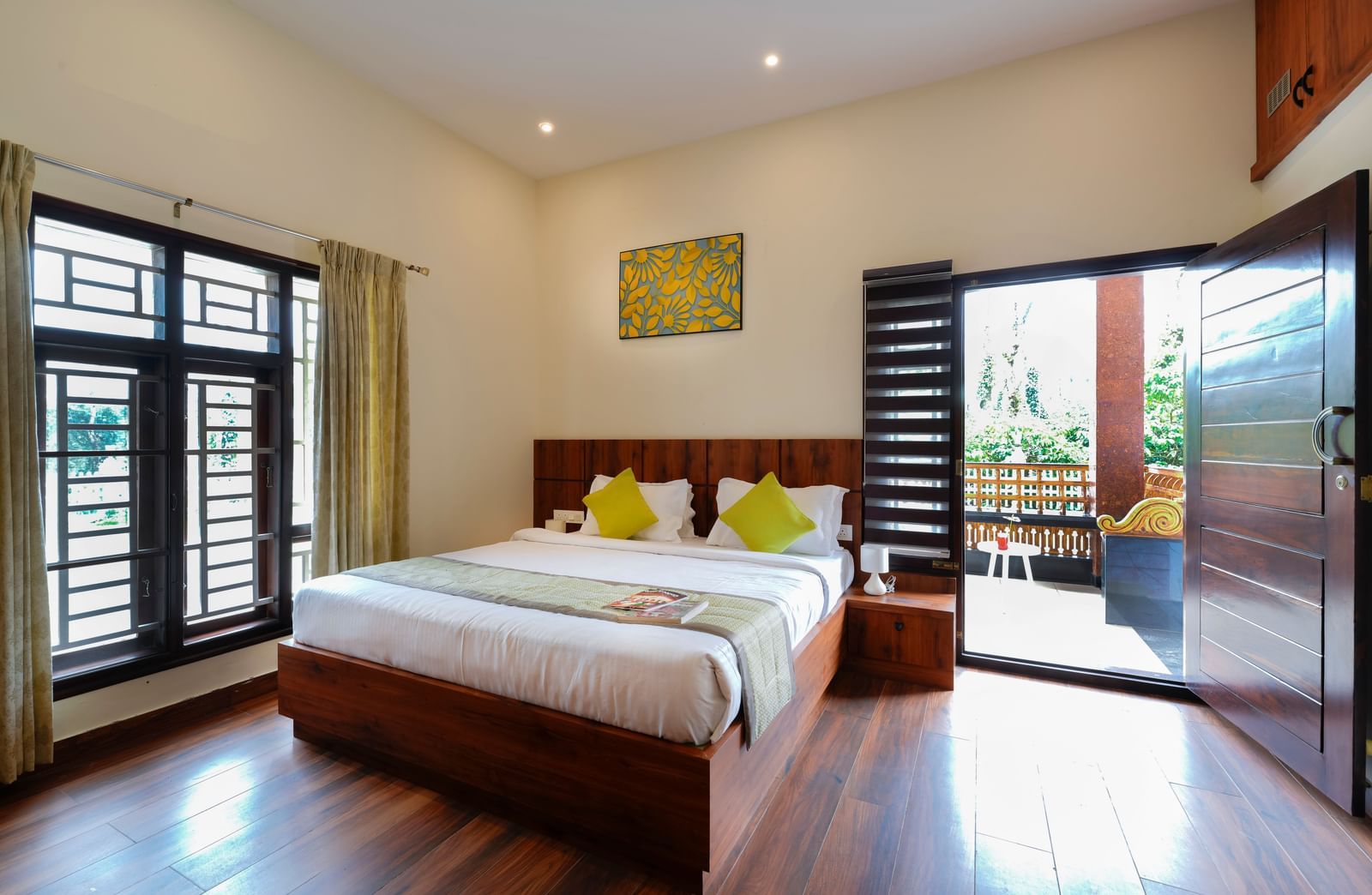  A premium room at Bhuthanakadu Retreat, featuring a large wooden bed with bright green and white bedding, and a sliding glass door leading to a balcony.