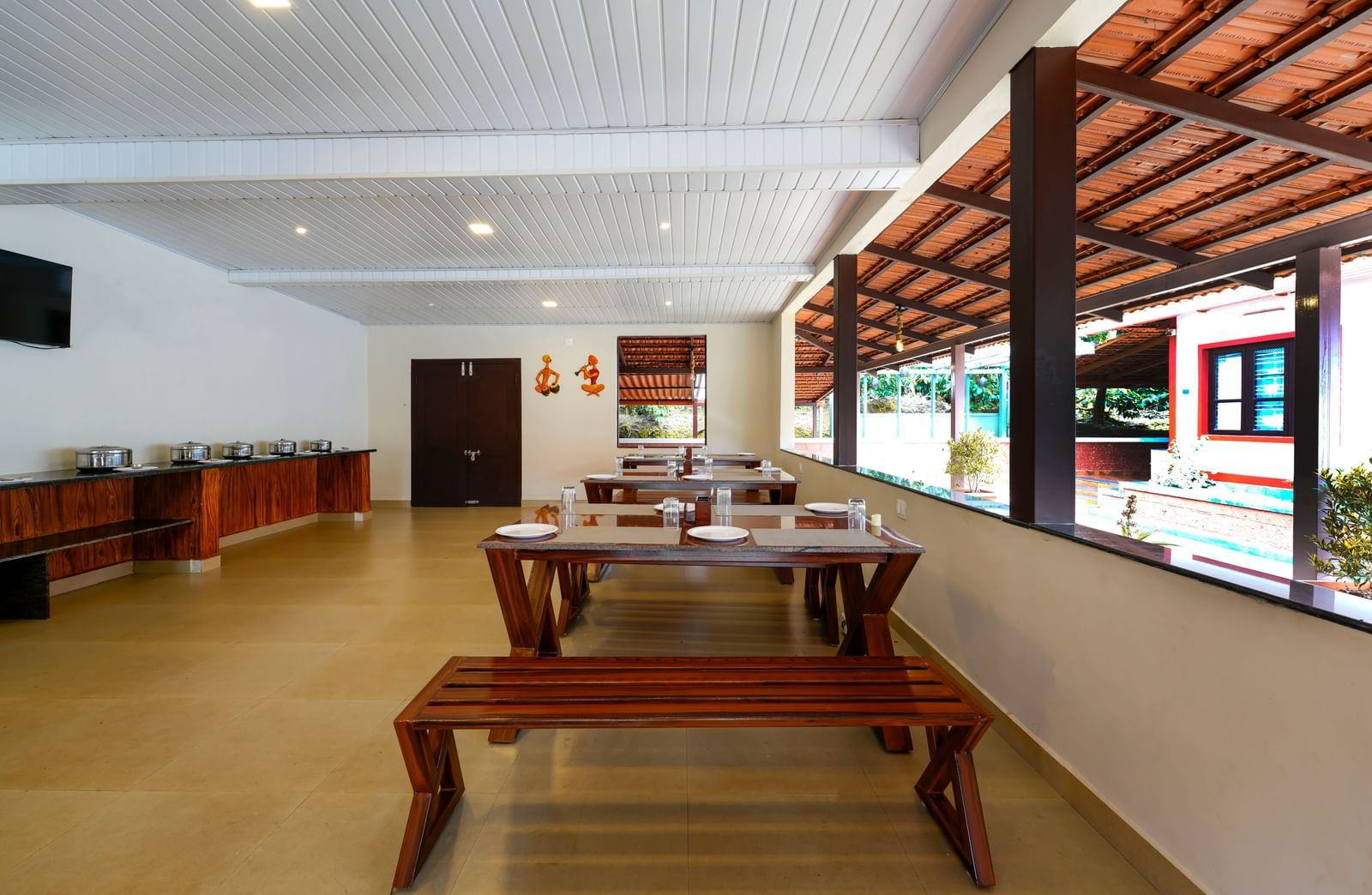A panoramic shot of the Mane Cafe at Bhuthanakadu Retreat, emphasizing the casual, inviting atmosphere of the dining area with a long serving station and windows overlooking the outdoors.