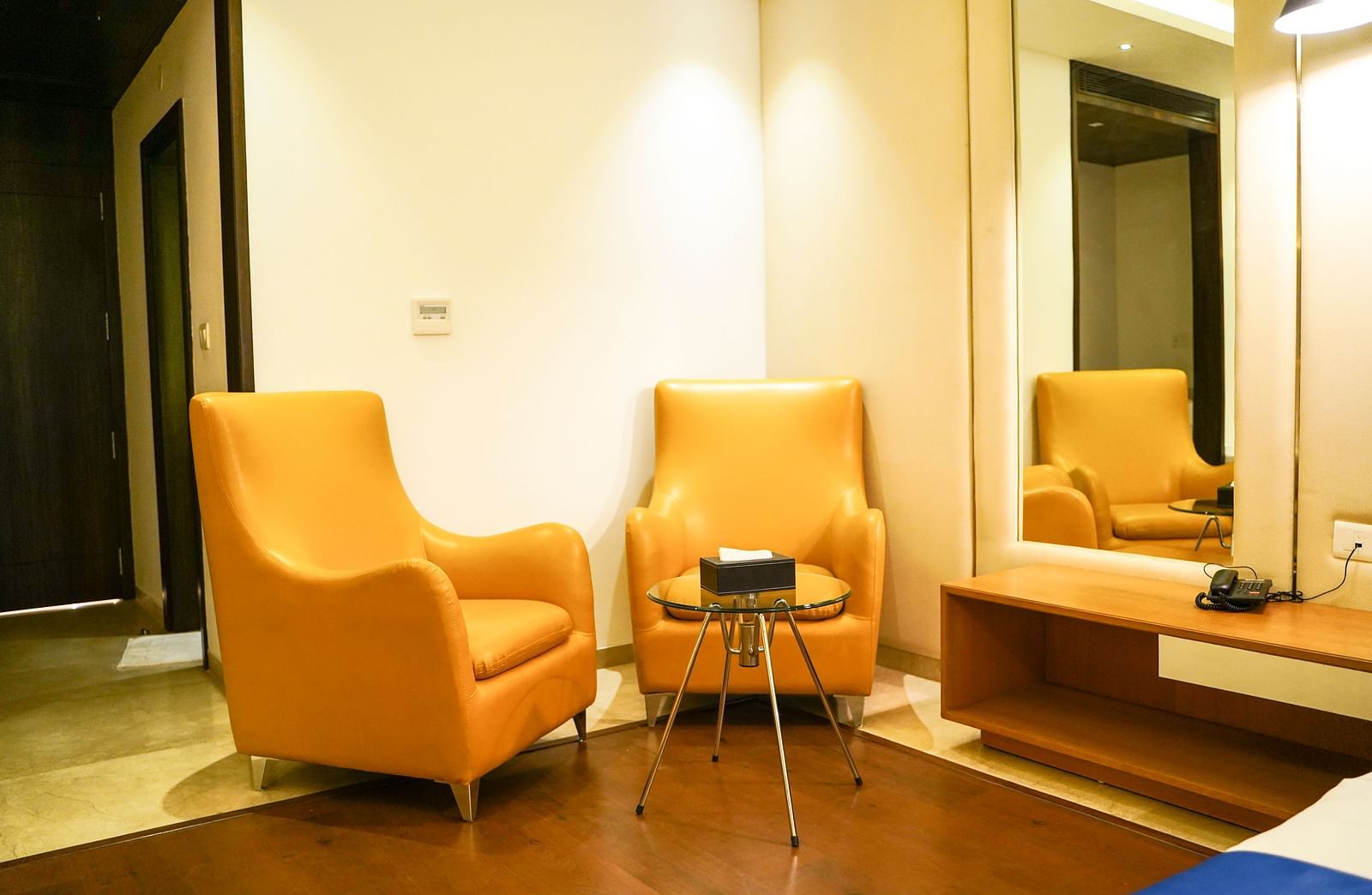  A cosy and inviting lounge area within BNGV Grandeur Hotel and Banquets, showcasing two comfortable orange armchairs and a small table, ideal for relaxation.