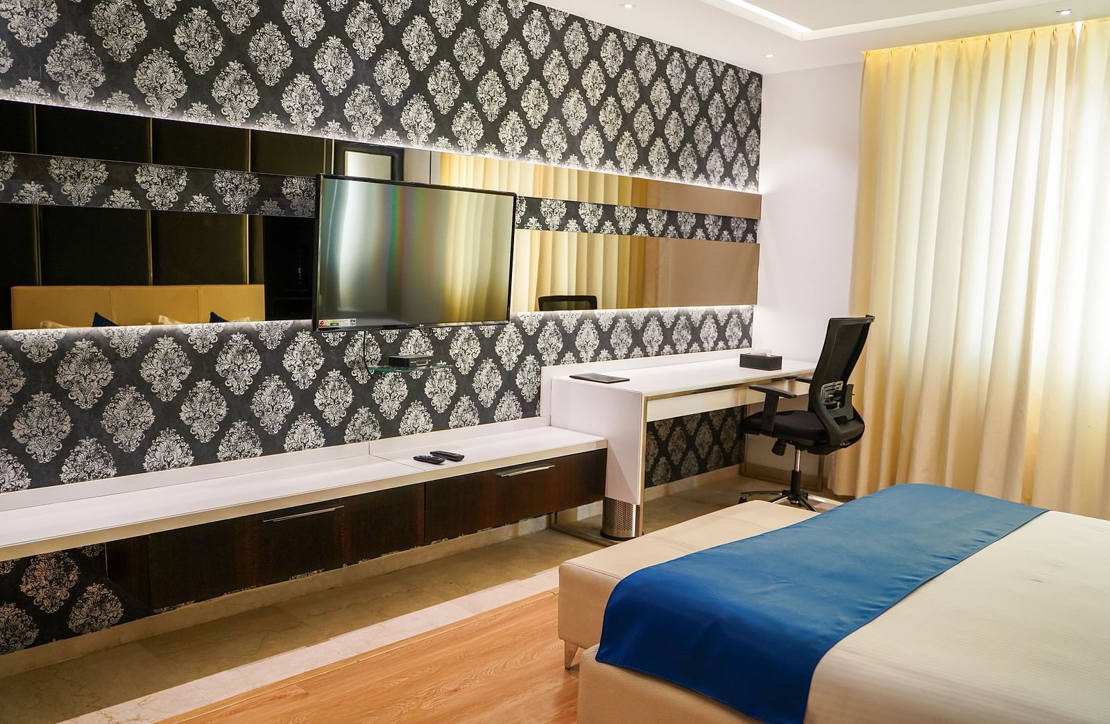 A functional and aesthetically pleasing hotel room at BNGV Grandeur Hotel and Banquets, featuring a comfortable bed, a desk with a chair, and elegant decor.
