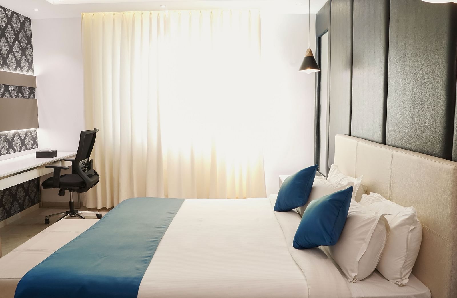 A contemporary hotel room at BNGV Grandeur Hotel and Banquets, offering a comfortable bed, a functional desk with a chair, and sleek, minimalist decor.