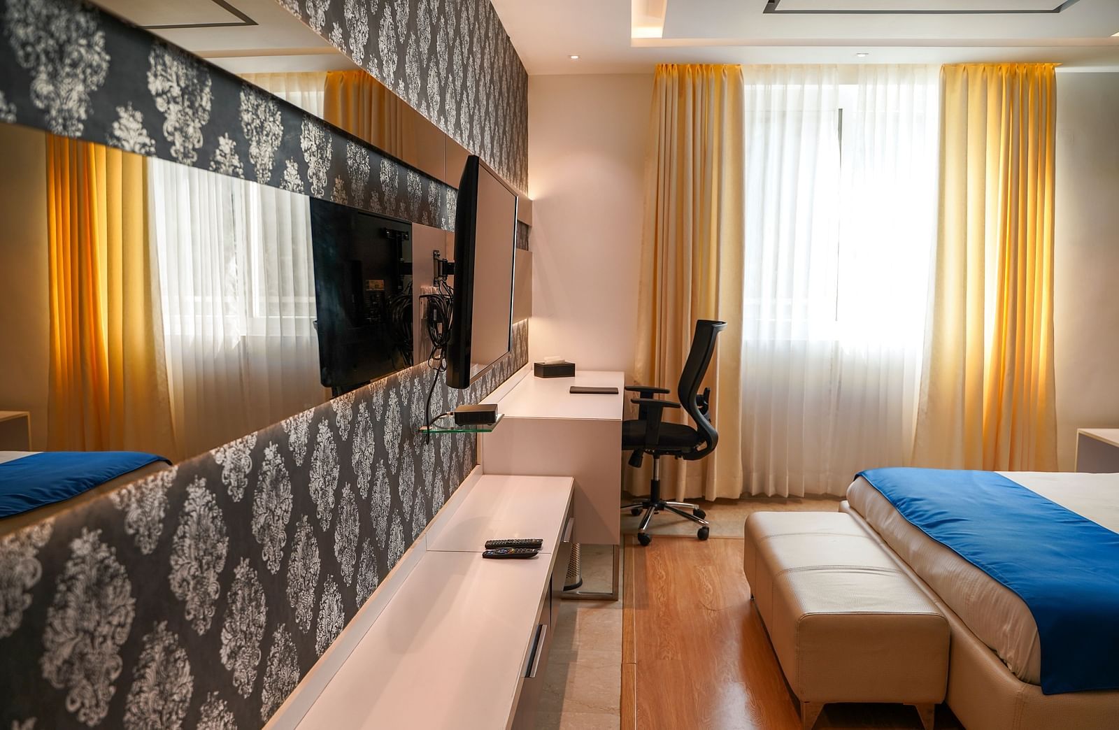 A well-appointed hotel room at BNGV Grandeur Hotel and Banquets, showcasing a bed, a patterned accent wall, a dresser, and a flat-screen TV.