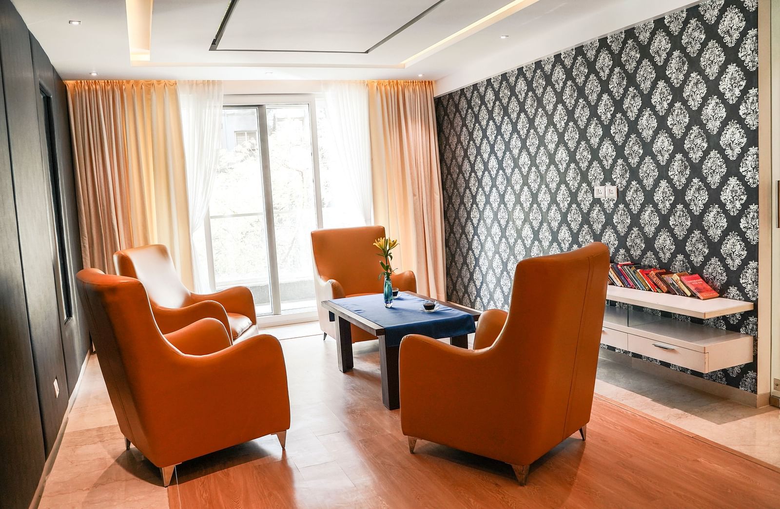 A stylish living area at BNGV Grandeur Hotel and Banquets, featuring comfortable orange armchairs, a coffee table, and a contemporary patterned accent wall.