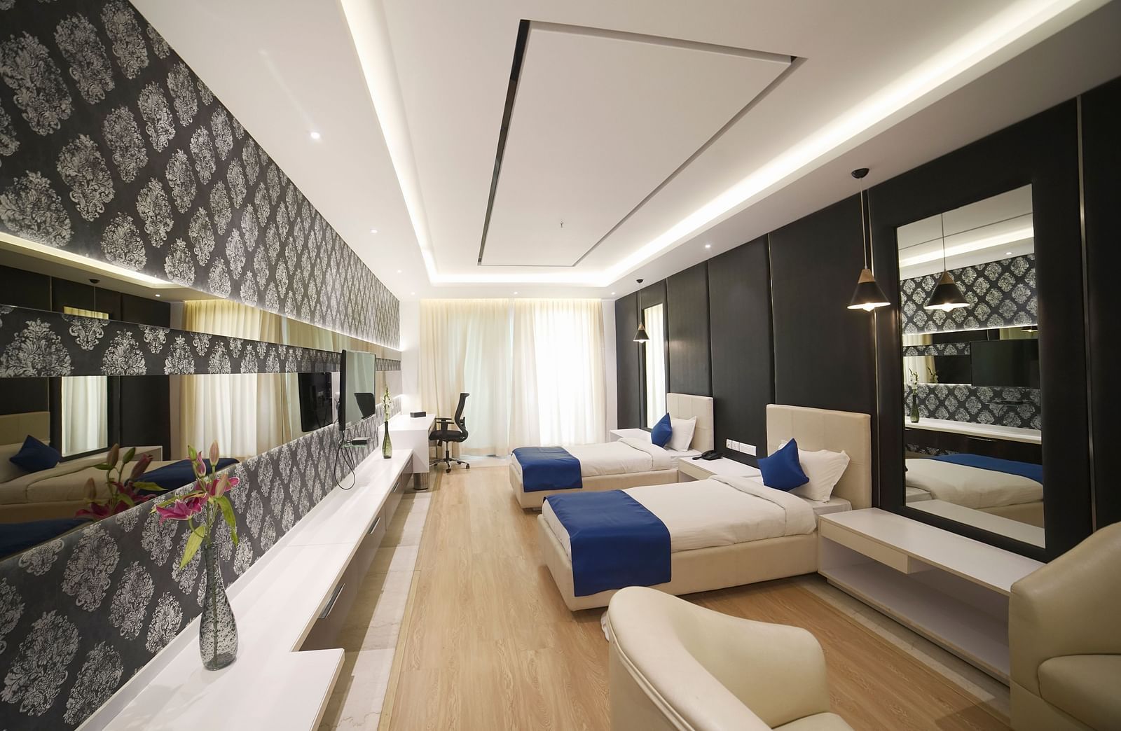  A stylish hotel room at BNGV Grandeur Hotel and Banquets, showcasing a bed with a blue runner, a patterned accent wall, and well-designed lighting.