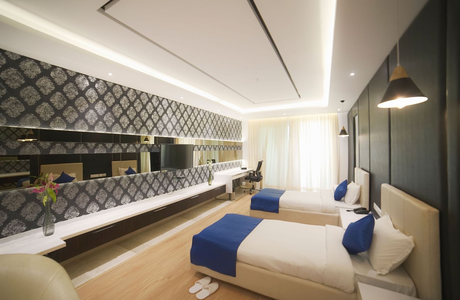 A clean and well-appointed hotel room at BNGV Grandeur Hotel and Banquets, featuring a bed with blue accents and an intriguing patterned wall design.