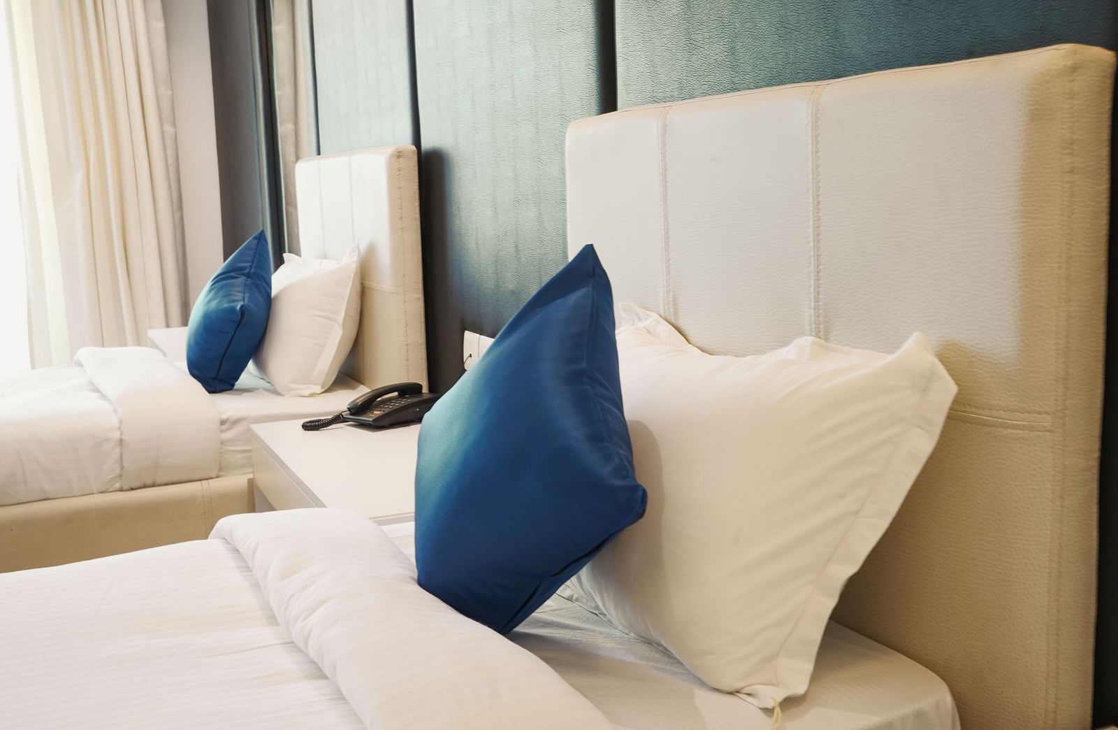 A close-up view of a comfortable bed in a hotel room at BNGV Grandeur Hotel and Banquets, highlighting the soft pillows and blue decorative cushion.