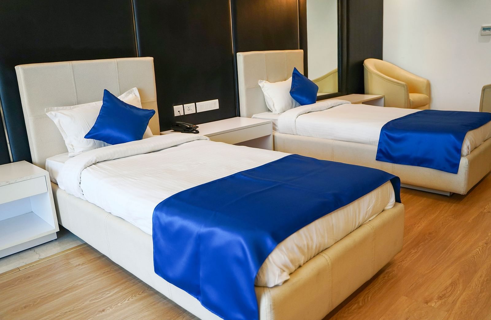 A bright and inviting hotel room at BNGV Grandeur Hotel and Banquets with two beds, each adorned with crisp white linens and a royal blue bed runner.