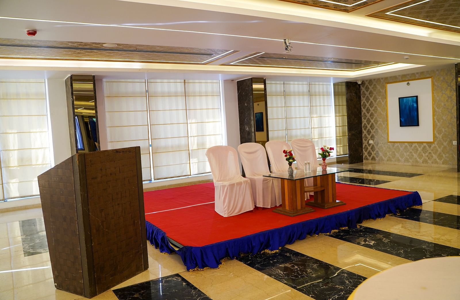 A well-lit smaller space at BNGV Grandeur Hotel and Banquets, arranged for an event with tables, chairs, and a podium.