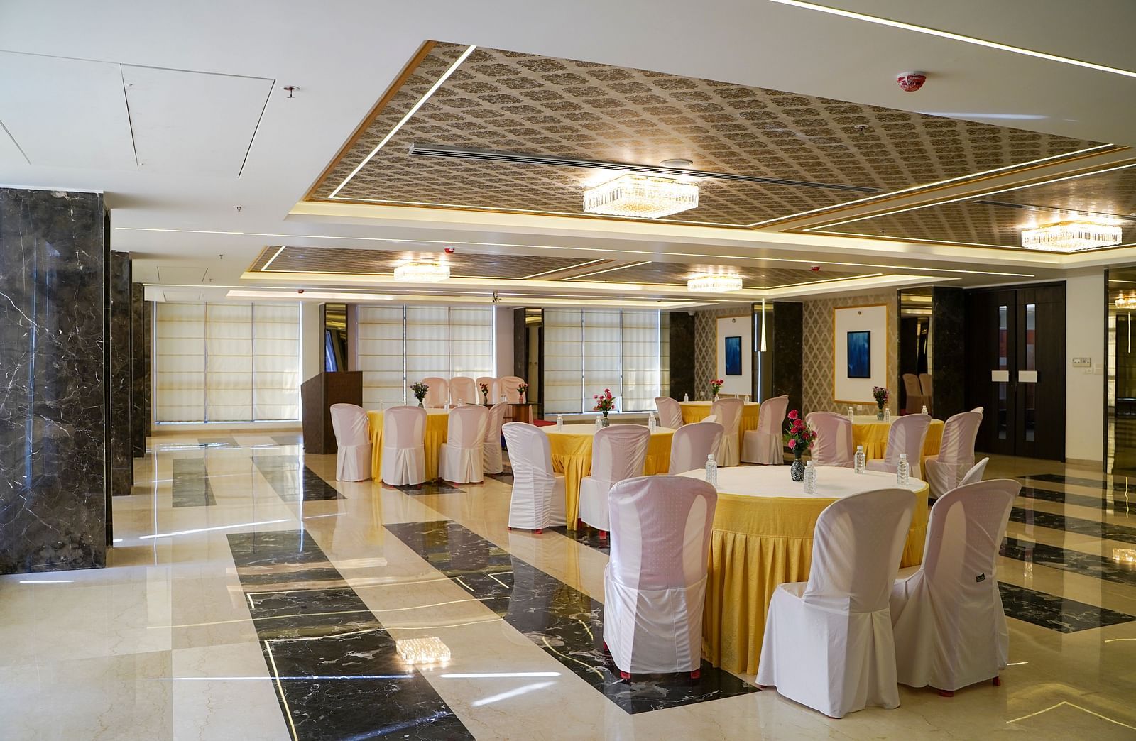 A large, elegant banquet hall with round tables draped in white, and chairs, set up for an event. The floor has a patterned tile design.
