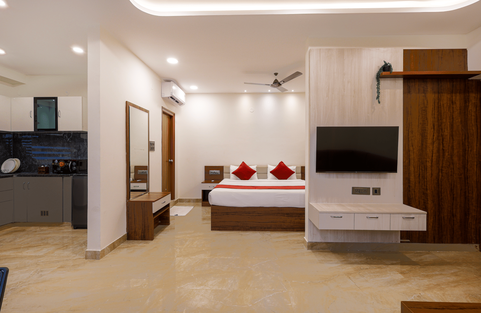 A room at Elysium Studio Suites, Madhapur, shows a bed, a wooden cabinet, and a television mounted on the wall.
