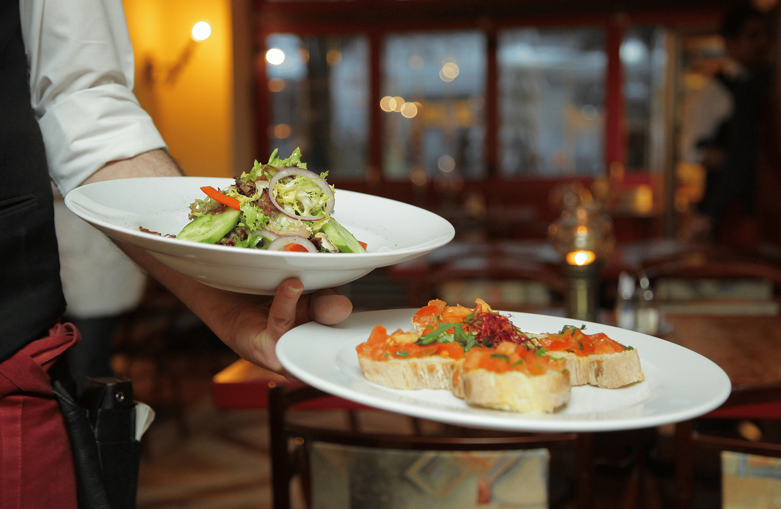 a person in a restaurant holding two plates with delicious cuisines in it that are well plated