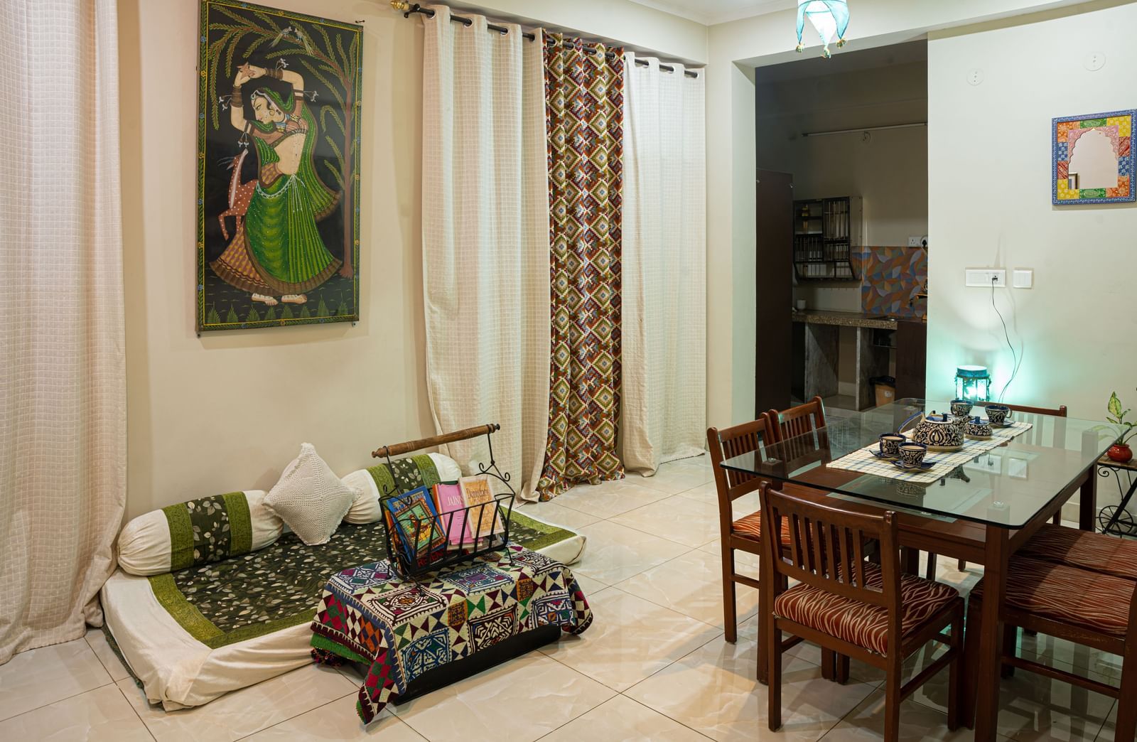 Indoor living space with low seating, dining table, wall painting, and curtains at Jaypore360 Homestay in Jaipur.