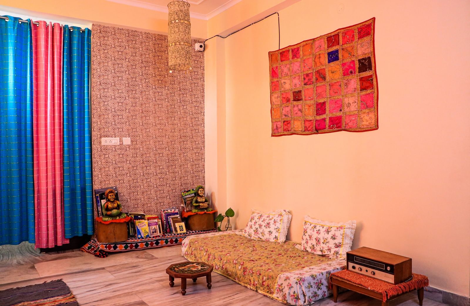 A room with a low bed, cushions, wall hanging, floor seating, and decorative elements on shelves at Jaypore360 Homestay in Jaipur.