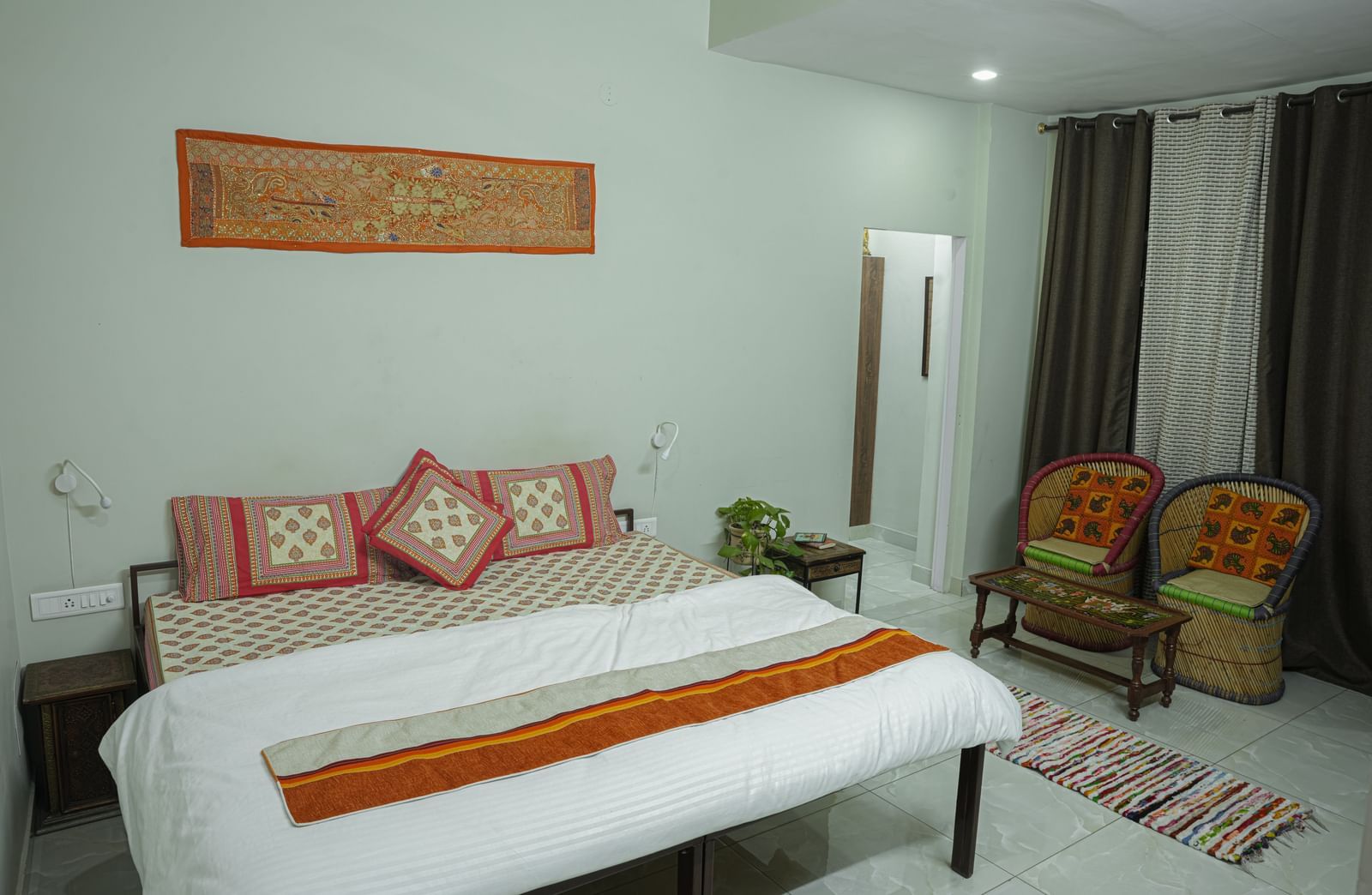 A well-kept bedroom with a double bed, white bedding, orange throw, chairs and wall decor at Jaypore360 Homestay - Best Rooms in Jaipur.