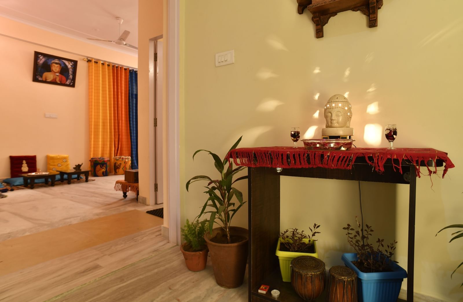 A small indoor shrine with lit lamps, plants, and decorative items arranged on a wall-mounted shelf at Jaypore360 Homestay in Jaipur.
