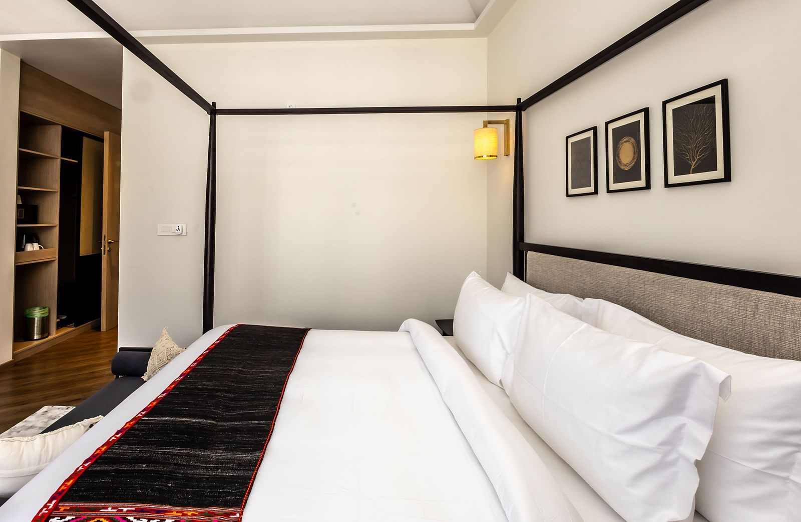 Four-poster bed with neatly made bed and wall mounted photoframs above the head board at Nivasana Manali.