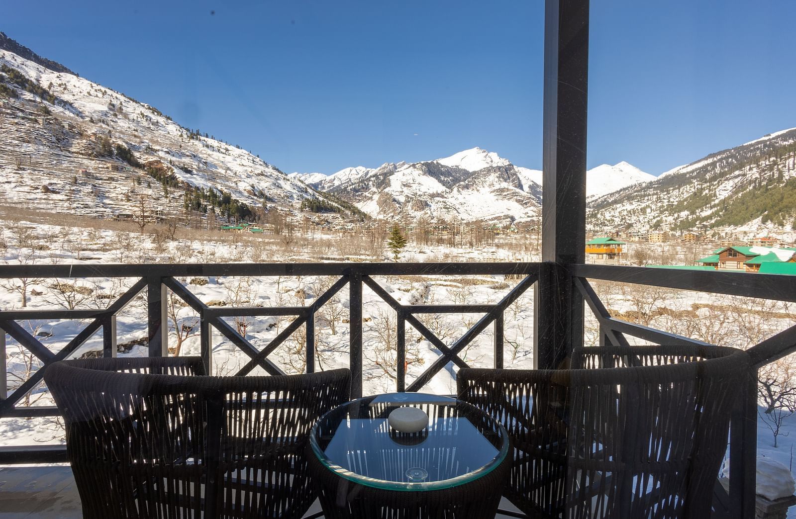 Balcony featuring wire chairs on either side of a short glass table, offering Himalayan views at Nivasana Manali.