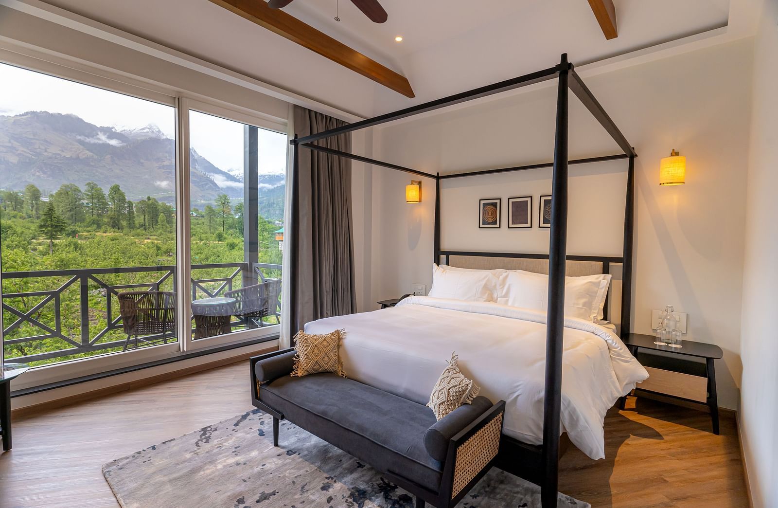 Spacious wooden-framed bed with seating at the foot and a large glass door opening to mountain views at Nivasana Manali.