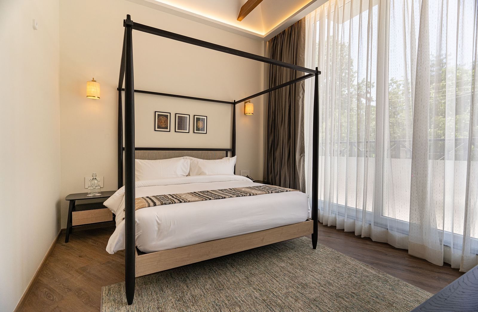 Room with wooden-framed bed and large curtained doors leading to balcony at Nivasana Manali.
