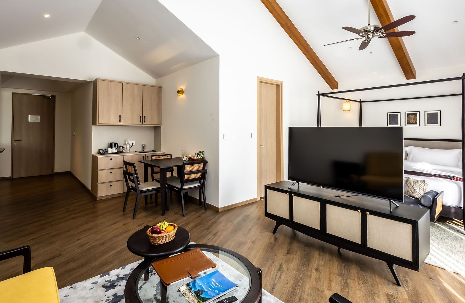 Diagonal view of the living area with a television, sofa, and kitchen area to wards the side at Nivasana Manali.