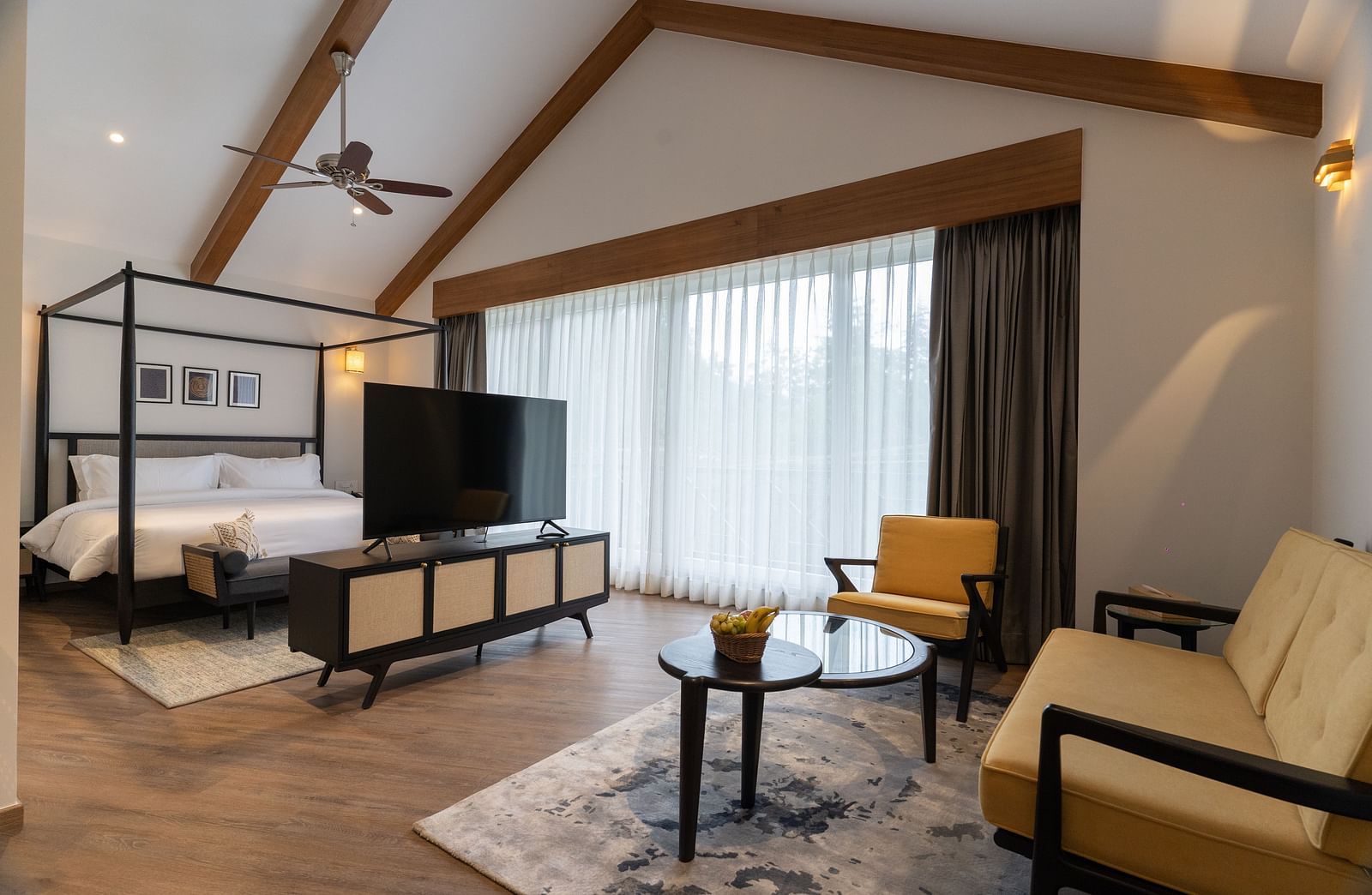 Spacious room with wooden-framed bed, cushioned sofa, and a TV placed on a wooden table at Nivasana Manali.