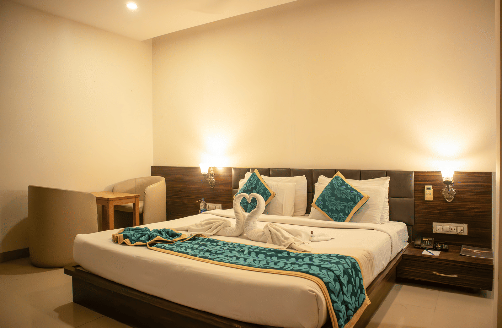 Deluxe Room of Papaya Tree Hotels furnished with double bed, a small lounge area with 2 armchairs and a coffee table, and 2 overhead lamps glowing.