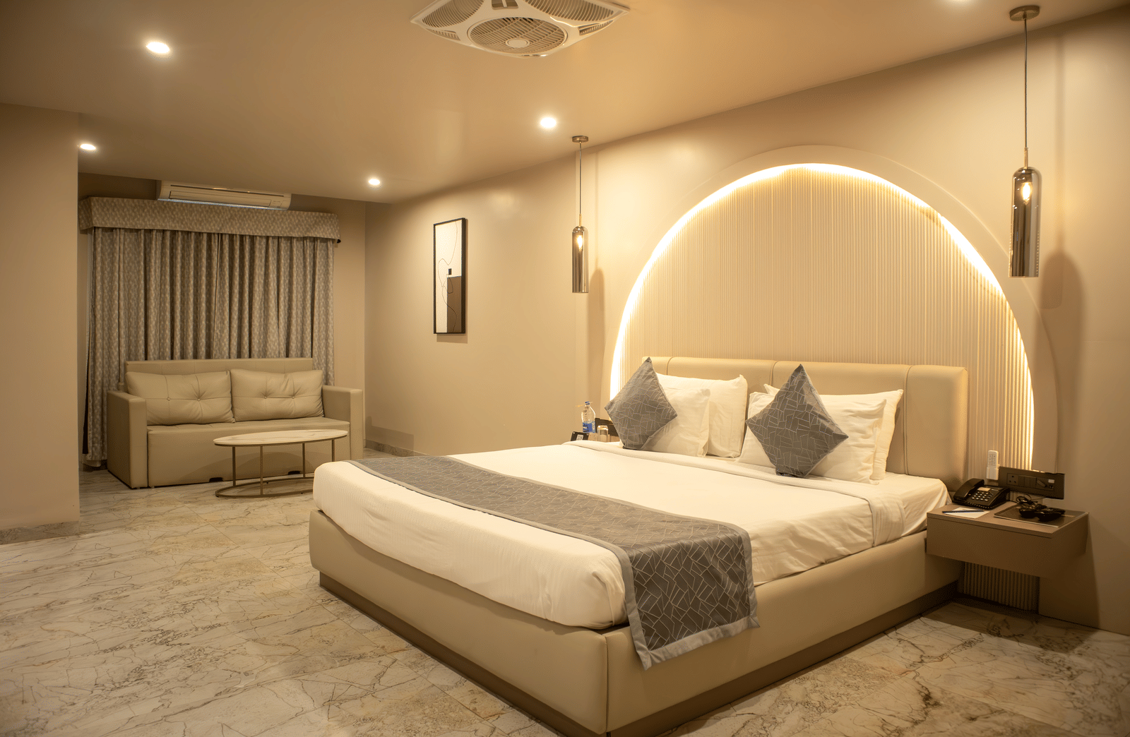 Wide view of bedroom at Papaya Tree Hotels Suite furnished with a double bed, a double-seating sofa, and and a bedside table. 