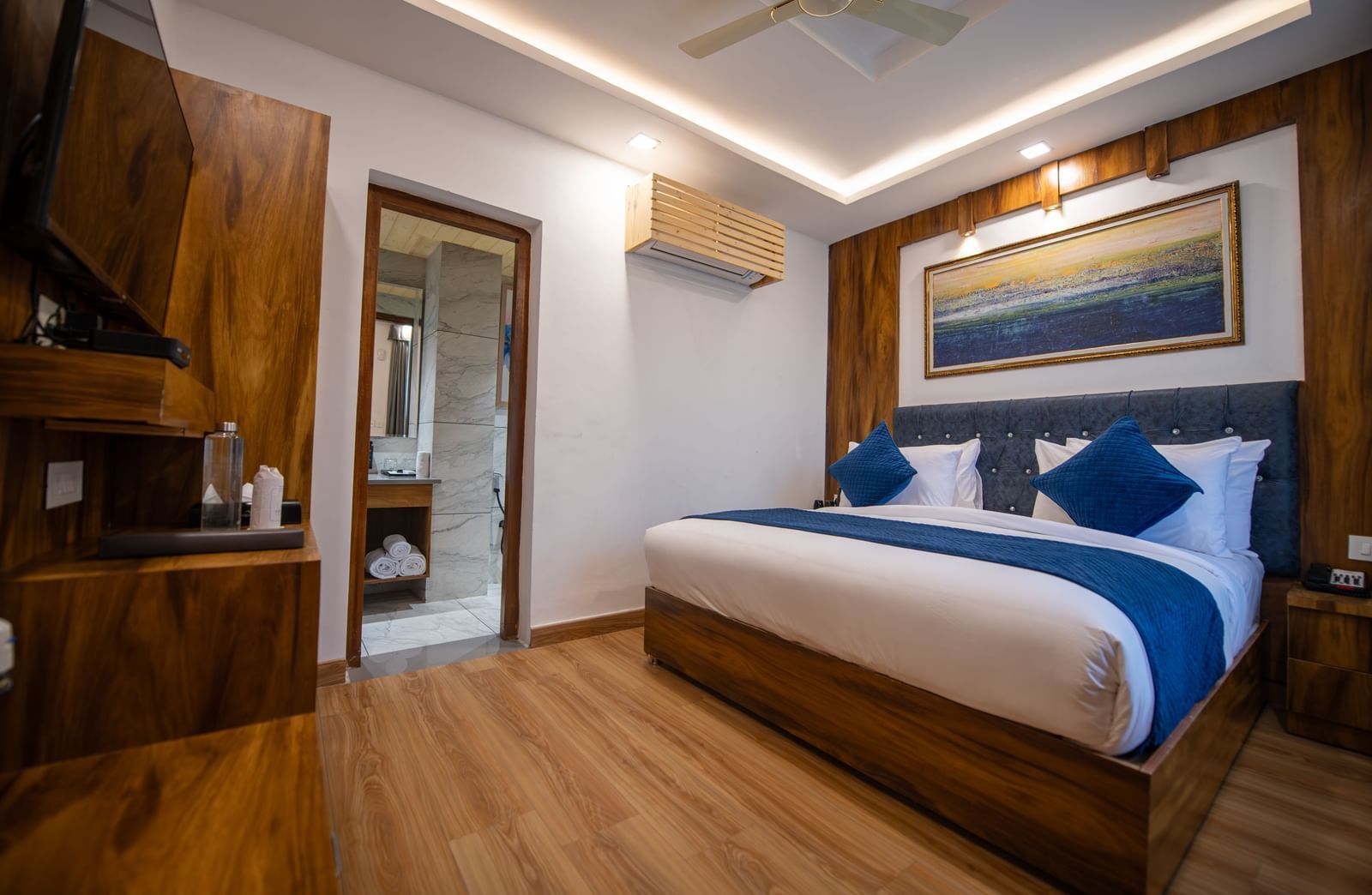A standard room at The Tattva Devaprayag with a bed featuring blue blankets and two pillows and an open bathroom door.