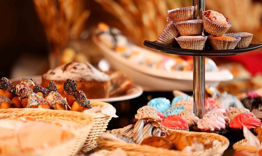 A close-up shot of a buffet table laden with a variety of pastries, including cupcakes on a tiered stand, decorated muffins, and other baked goods in wicker baskets - UDS Group of Hotels.