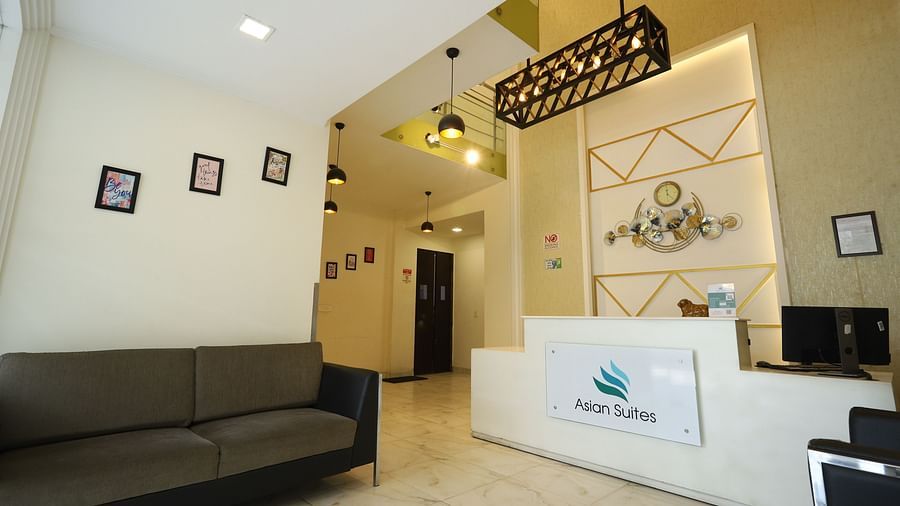 A reception area with a dark sofa and a white counter featuring a logo, illuminated by modern lighting fixtures - Asian Suites Cyber Park, Gurgaon