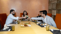 A group of people dining and conversing at a restaurant table at Park Plaza Ludhiana with padded terracotta wall panels warm lighting and food placed on the table.