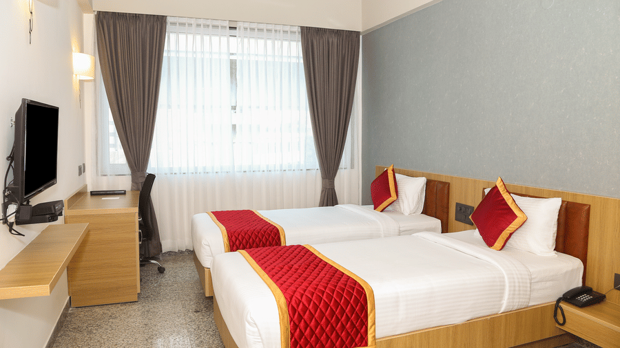Two single beds, a window with curtains, and a wooden desk at Icon Express By Bhagini, Mahadevapura.