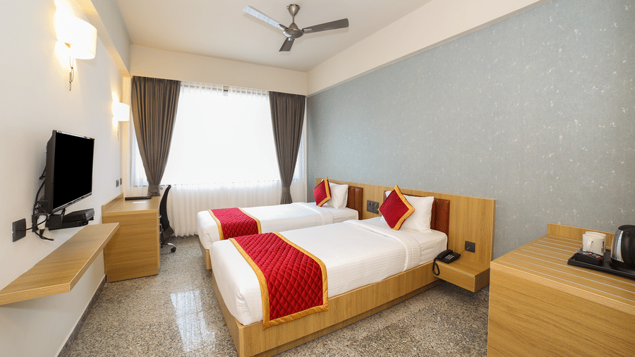 Two single beds, a wall-mounted television, and a wooden desk at Icon Express By Bhagini, Mahadevapura.