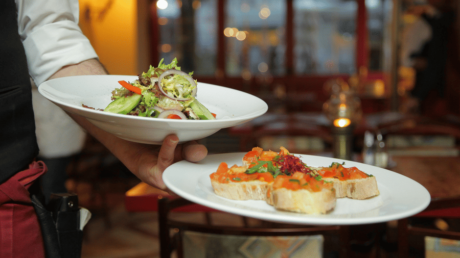 a person in a restaurant holding two plates with delicious cuisines in it that are well plated