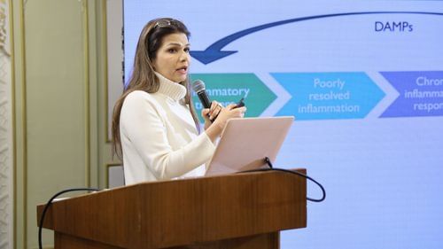 An image of a woman standing on a podium with a microphone in her hand giving a speech at Heritage Village Resorts & Spa