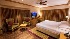 A room with a double bed, wooden furniture seating area with green & brown accents at The Clarton. One of the finest Kodaikanal rooms near lake.