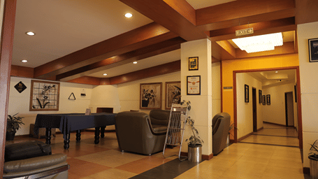 Lounge at Benzz Park with a pool table, leather sofas, framed artwork on the walls, a wood beamed ceiling and a corridor leading toward the guest rooms.